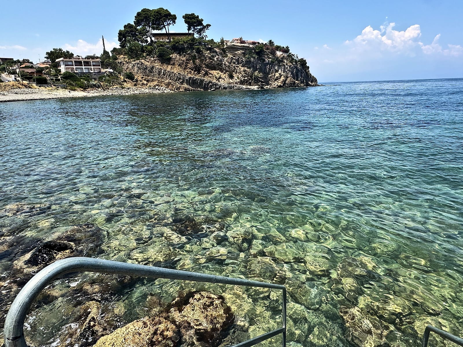 Acqua cristallina tra gli scogli della baia, con la scaletta per entrare in mare