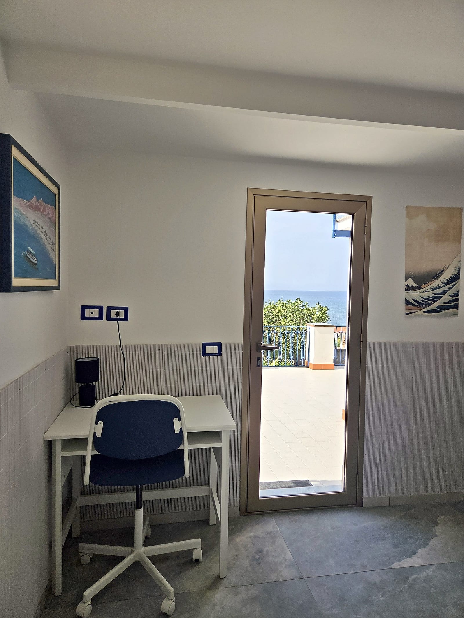Scrivania con sedia blu accanto alla porta a vetri aperta sulla terrazza e sul mare